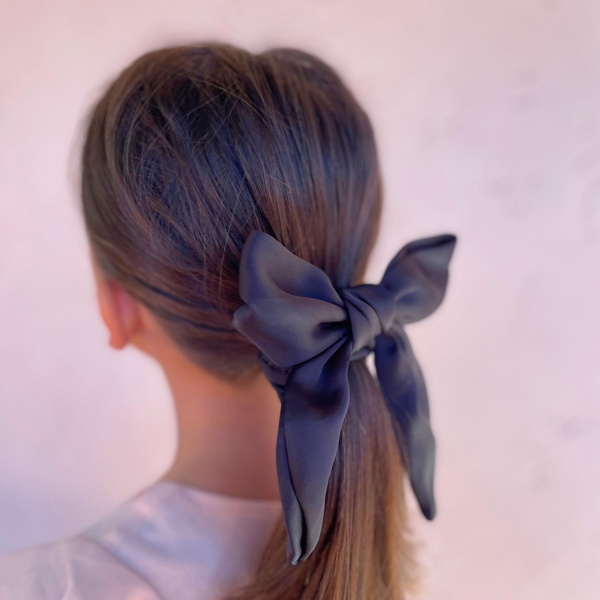 Kids satin scrunchie with an attached bow, providing a comfortable hold and a touch of elegance to everyday hairstyles.